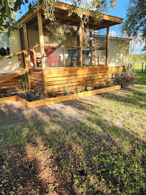 Una estructura de madera con un porche cubierto, mobiliario exterior y bancales elevados.