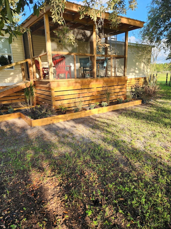 A wooden structure with a covered porch, outdoor seating, and raised garden beds.