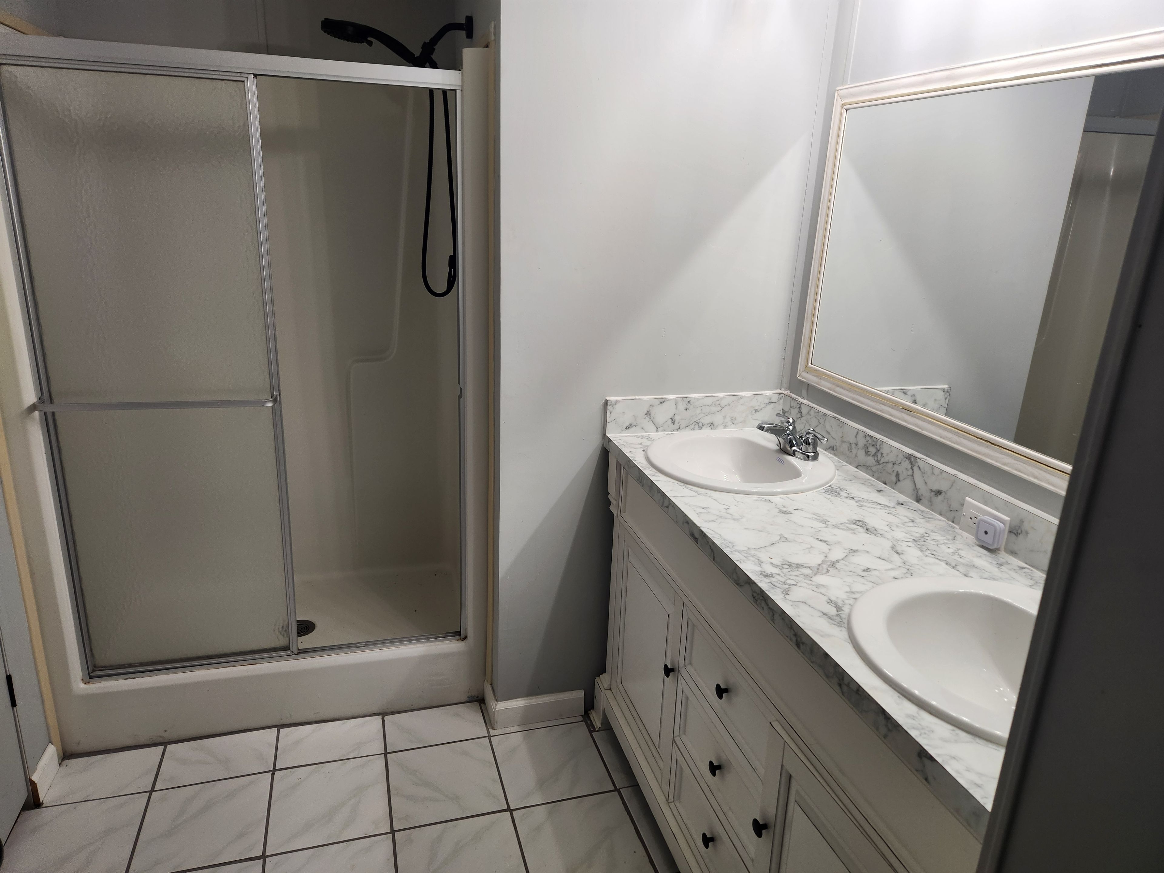 A bathroom with a glass-enclosed shower, two sinks with marble countertops, and a large mirror.