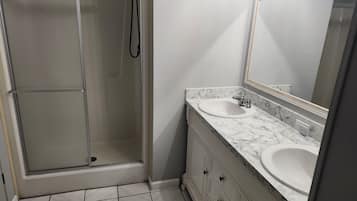 A bathroom with a glass-enclosed shower, two sinks with marble countertops, and a large mirror.