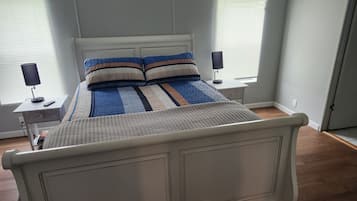 Una cama con cabecera, dos mesitas de noche con lámparas y una ventana con persianas.