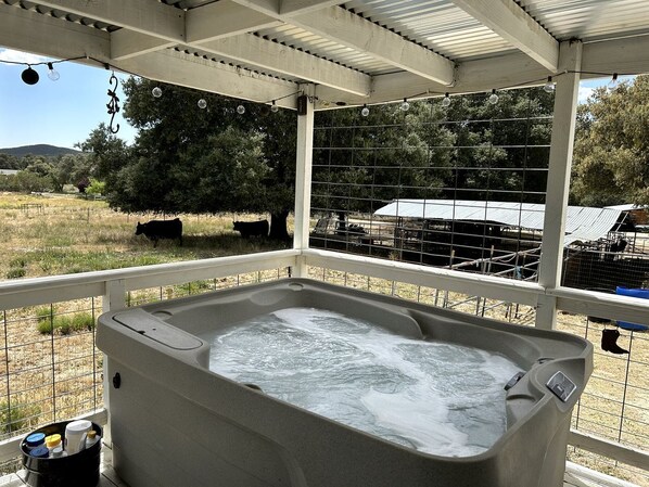 A hot tub under a covered patio with a view of a fenced area and trees.