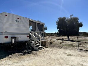 A mobile home with a staircase leading to a deck, surrounded by a fenced area and a tree.
