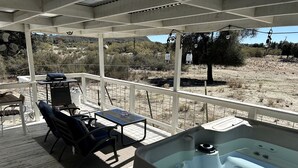 Eine überdachte Terrasse im Freien mit Whirlpool, Sitzgelegenheit und Blick auf die umliegende Landschaft.
