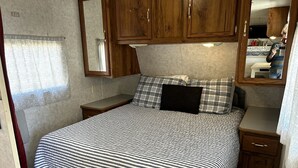 Ein Schlafzimmer mit einem Bett, Holzschränken, einem Spiegel und einem kleinen Nachttisch.