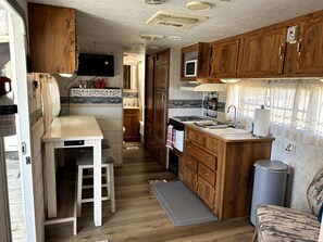 A compact RV kitchen with wooden cabinets, a sink, a stove, and a small dining area.