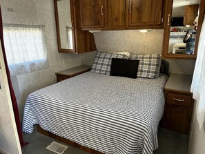 A bedroom with a bed, wooden cabinets, a mirror, and a small bedside table.