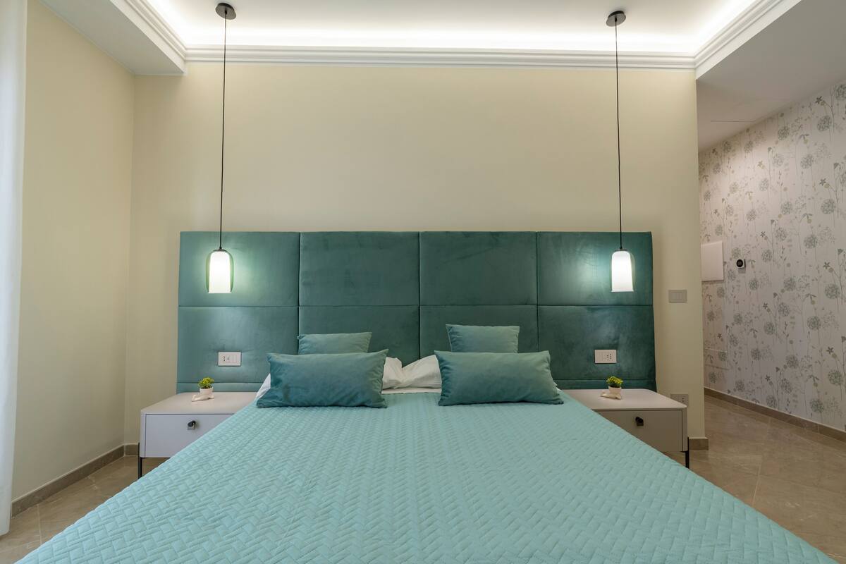 Un dormitorio con una cama grande, dos mesitas de noche y un cabecero con luces colgantes.