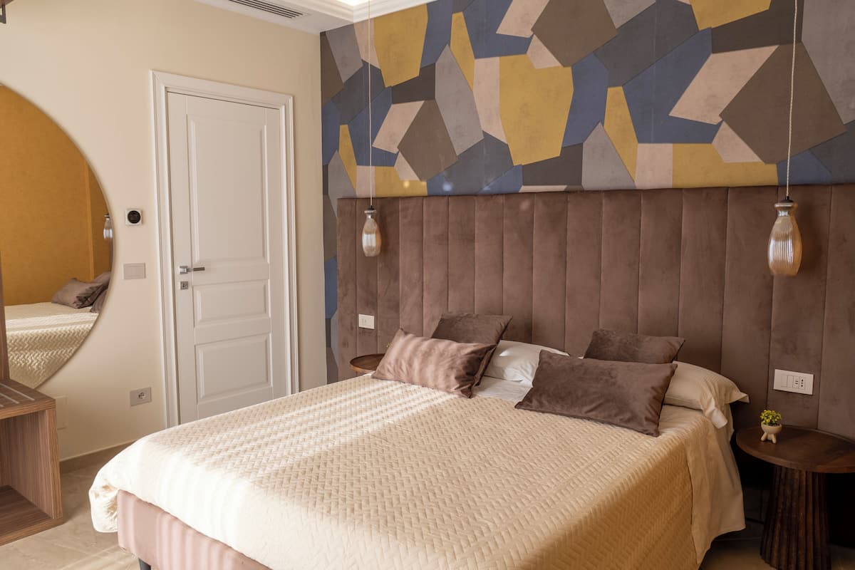 Un dormitorio con una cama grande, un cabecero con un diseño geométrico en la pared y un espejo redondo a la izquierda.
