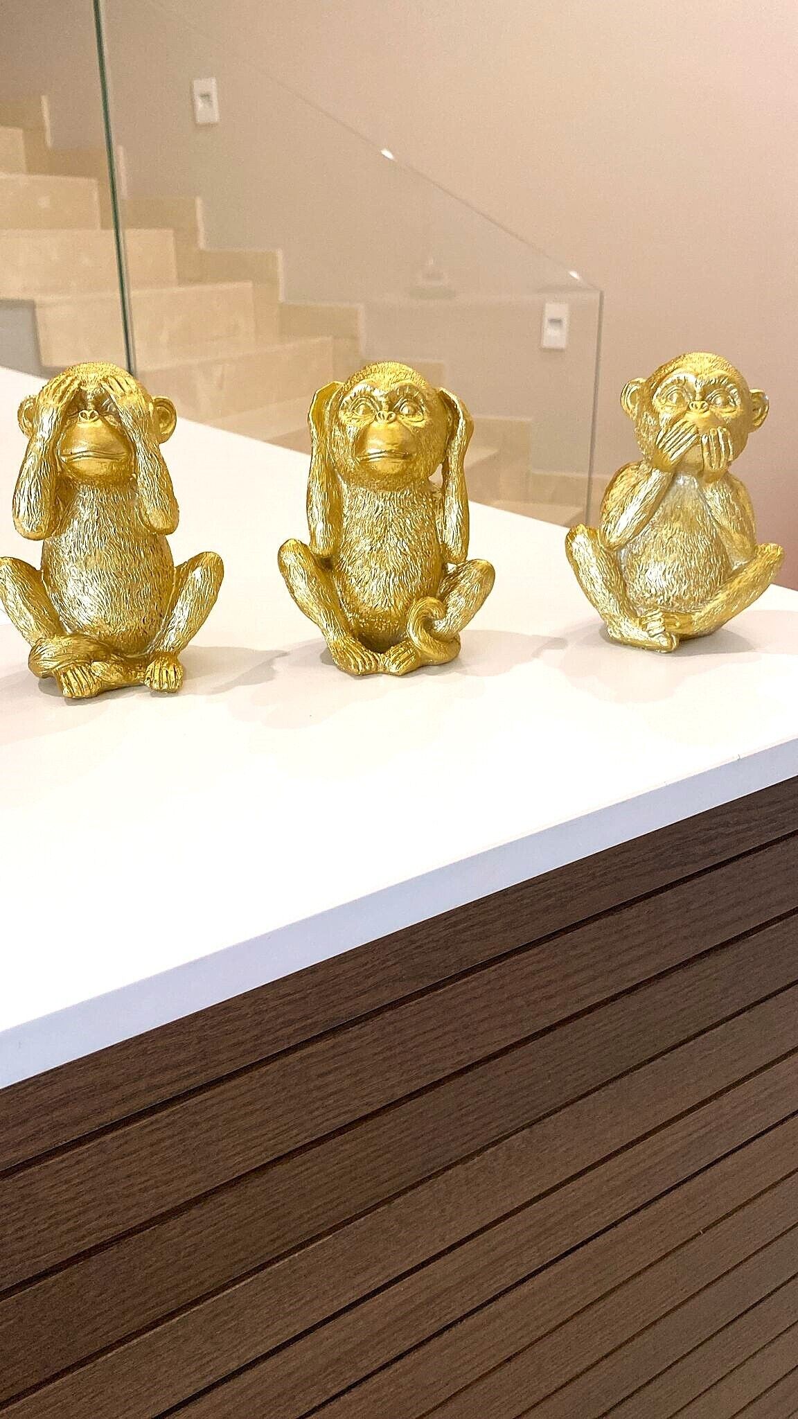 Three golden monkey figurines on a white surface.