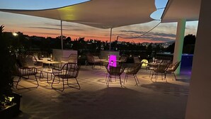 Un patio exterior con suelo hexagonal, una gran esfera iluminada y varias zonas de estar bajo una marquesina.