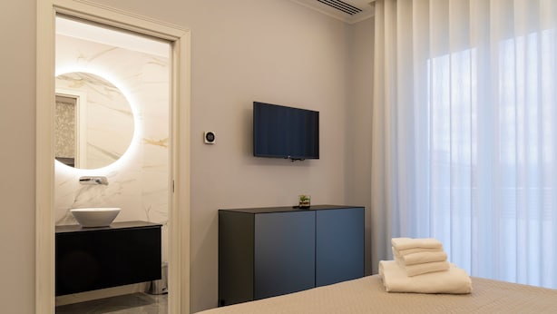 Un dormitorio moderno con cama, televisor, tocador con espejo y ventana con cortinas.