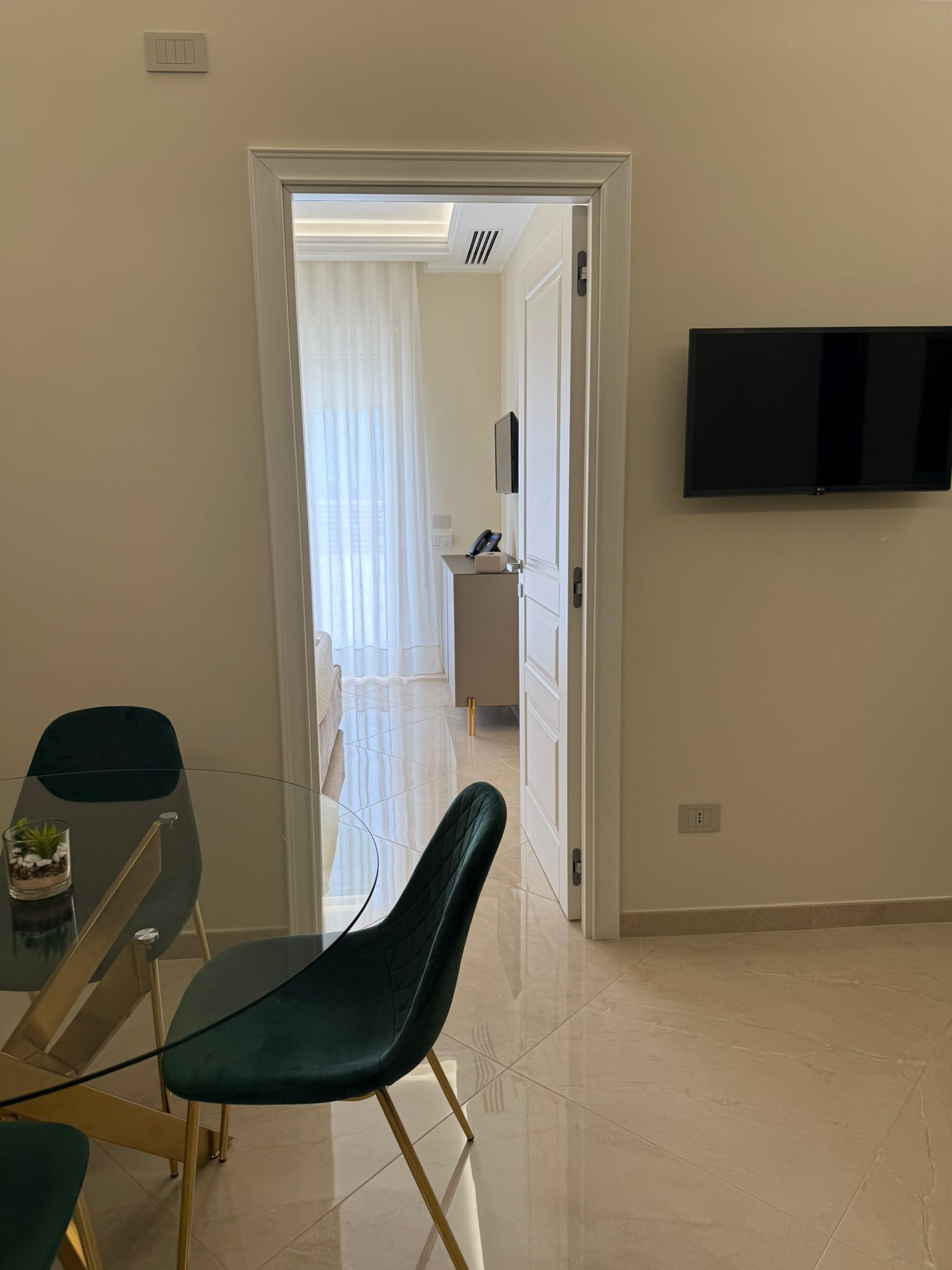 Une chambre d’hôtel moderne dotée d’un coin repas, d’un téléviseur fixé au mur et donnant sur la chambre adjacente.