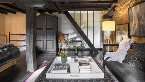 Een gezellige kamer met een houten trap, een bank, een bijzettafeltje met boeken en een lamp.