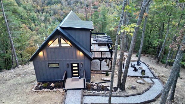 Eine Hütte mit geneigtem Dach, einer Terrasse und einem Kiesweg, der zum Eingang führt.