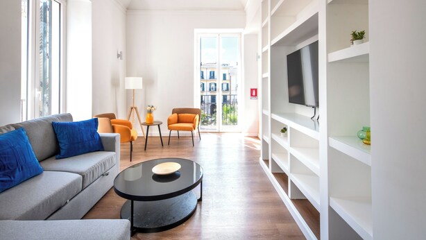 A modern living room with a grey sofa, blue cushions, a black coffee table, orange chairs, and a TV on a white shelf. - Ci' Capo Apartments by Wonderful Italy (Palermo)