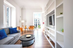 Un soggiorno moderno con un divano grigio, cuscini blu, un tavolino da caffè nero, poltrone arancioni e una TV su uno scaffale bianco.
