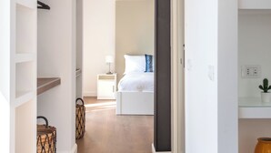 A hallway leading to a bedroom with a bed, bedside table, and a nightstand. There are built-in shelves on the left and a potted plant on the right. - Ci' Capo Apartments by Wonderful Italy (Palermo)
