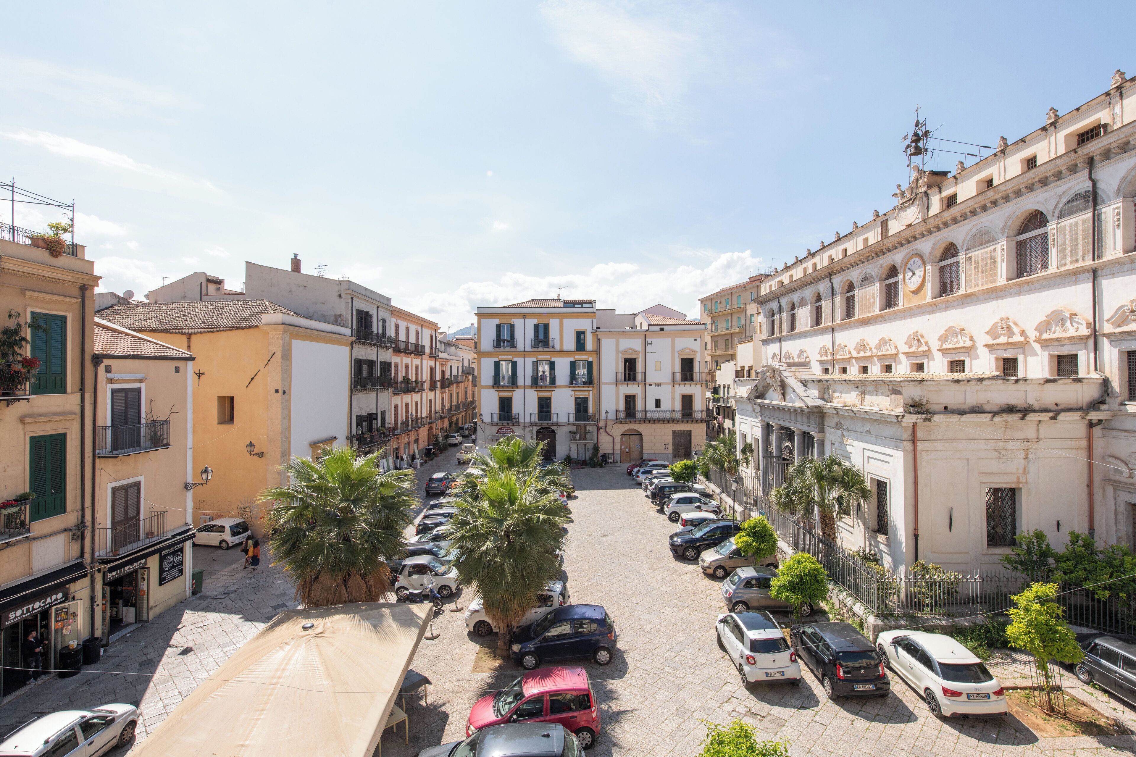 Vista da rua com carros estacionados, edifícios e céu claro.