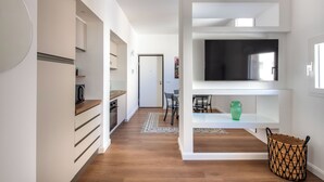 A modern kitchen with white cabinetry, a built-in oven, and a microwave. There is a dining area with a table and chairs, and a TV mounted on a white shelf. - Ci' Capo Apartments by Wonderful Italy (Palermo)