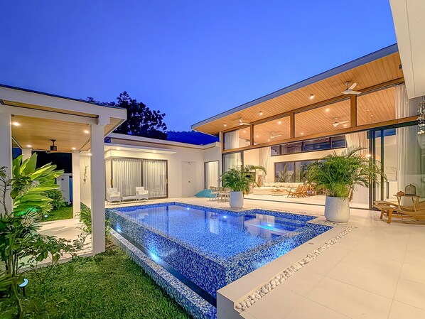 A modern house with a swimming pool, outdoor seating, and a large window overlooking the garden.