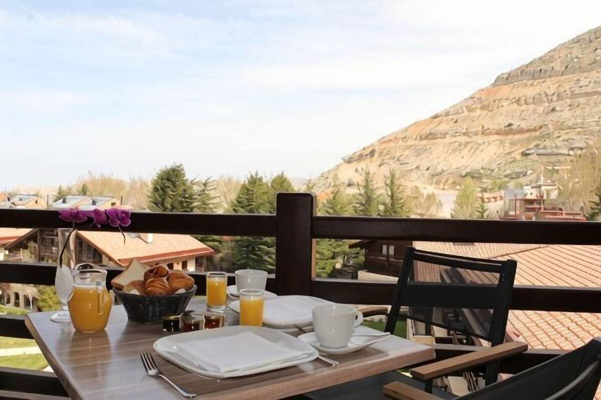Une table de petit-déjeuner avec du jus d’orange, des viennoiseries et une vue sur un paysage montagneux.
