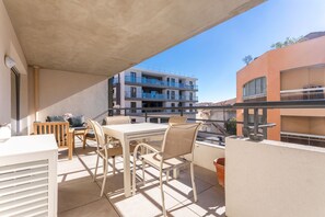 A balcony with a table and chairs, a potted plant, and a view of a multi-story building.