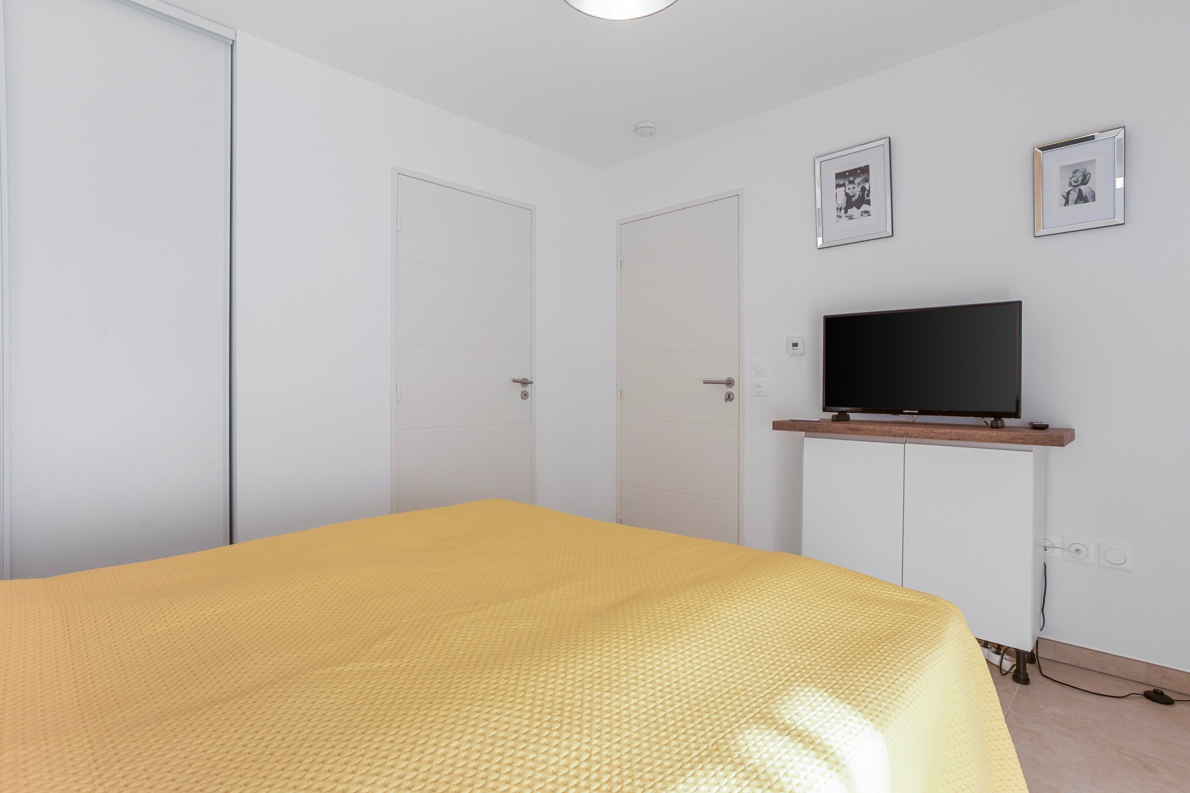 A bedroom with a bed, a television on a stand, and two doors.