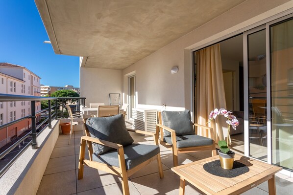 A balcony with two wooden chairs, a small table, and a potted orchid.
