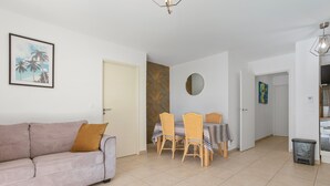 Een woonkamer met een bank, een eettafel met stoelen, een ronde spiegel en een kleine prullenbak.