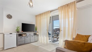 Een moderne woonkamer met een flatscreen televisie, een bank, een salontafel en een schuifdeur die leidt naar een terras.