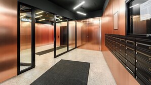 En modern entréhall för hissar med glasdörrar, ett svart golv och en väggmonterad brevlåda.