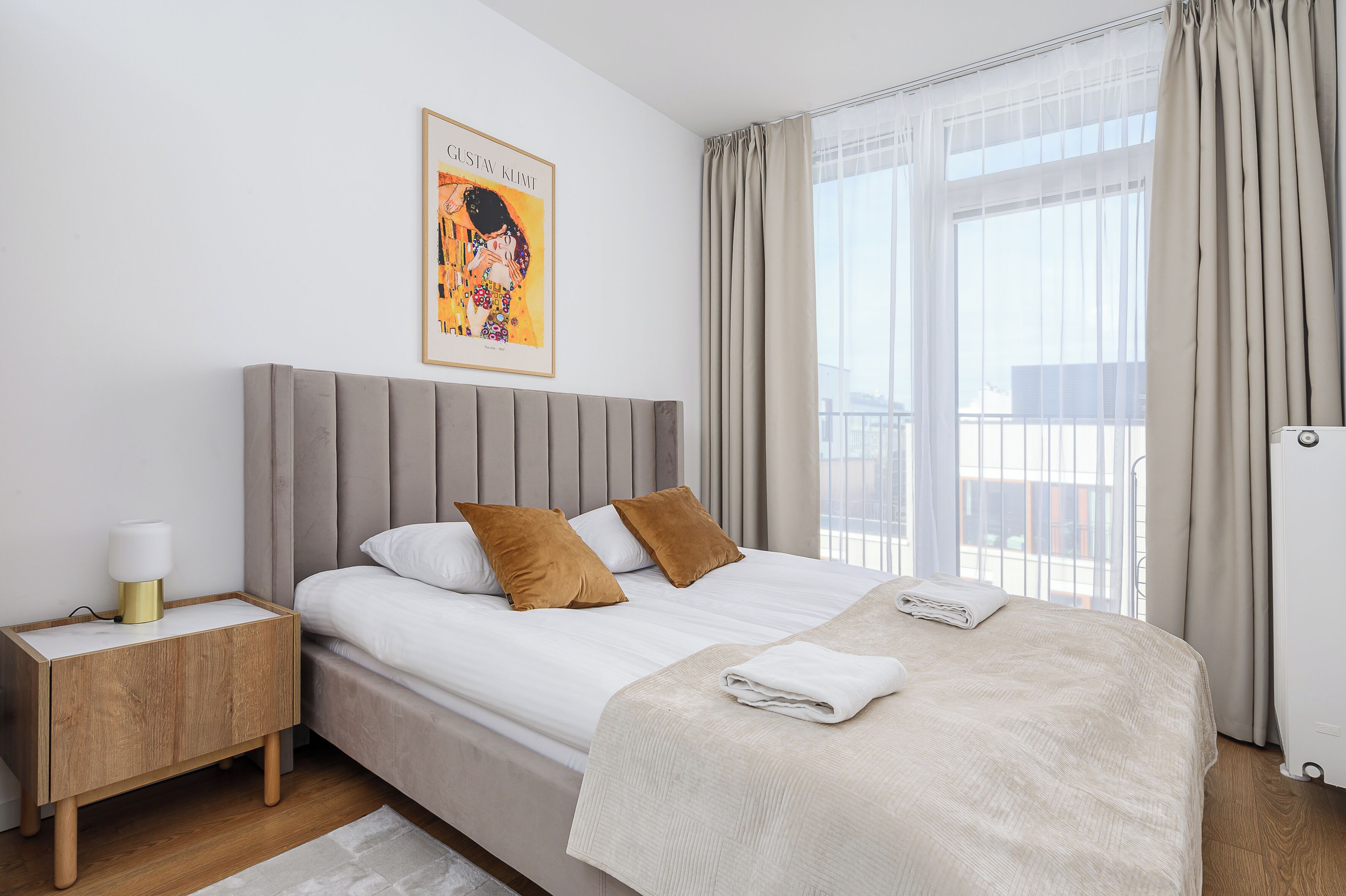 A neatly made bed with a headboard, a bedside table with a lamp, and a framed artwork on the wall.