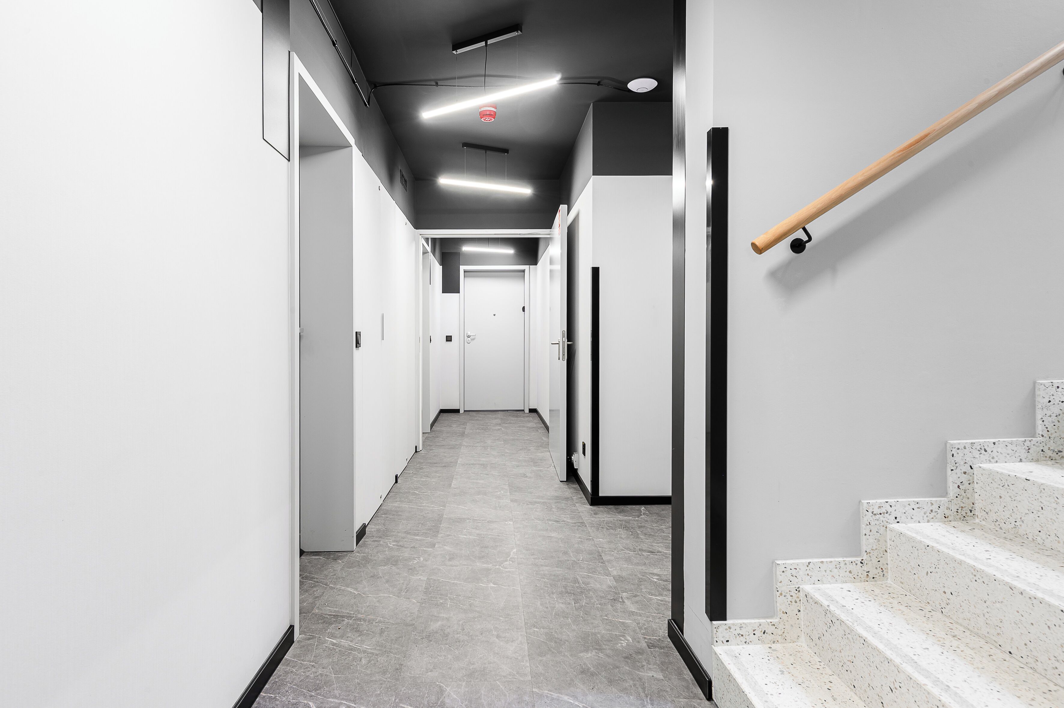 A modern hallway with a staircase on the right, leading to a door at the end.