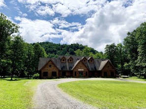 A rustic wooden building with a gravel driveway and a grassy field.