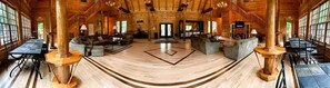 A spacious log cabin interior with a central seating area, a staircase, and large windows.