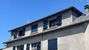 A two-story building with a flat roof, multiple windows with shutters, and a front entrance with a door. - Charming Mountain House in the Heart of the Pyrenees (Garin)