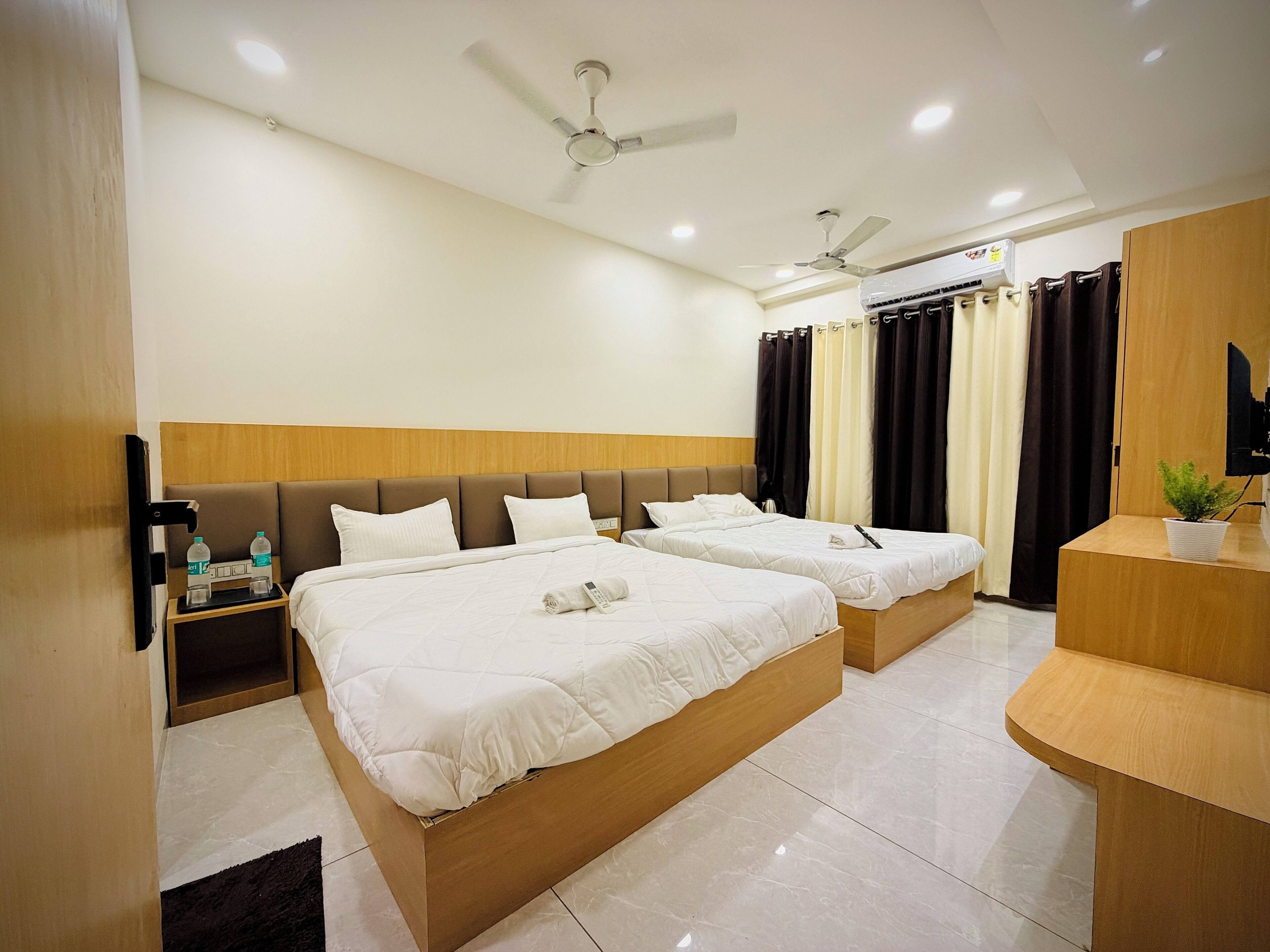 A hotel room with two beds, a wooden headboard, a ceiling fan, a TV, and a small plant.