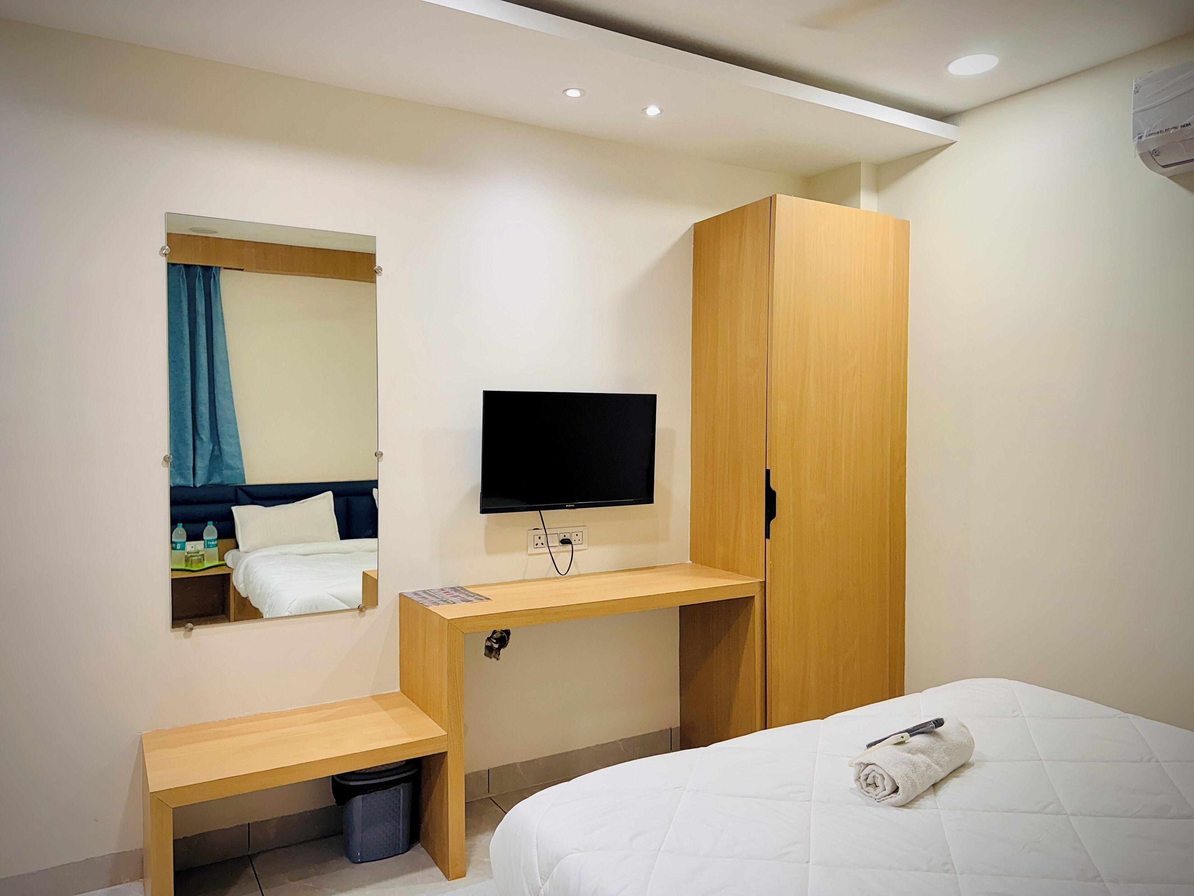 A hotel room with a bed, a wooden desk, a TV, and a wardrobe.