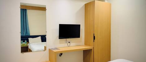 A hotel room with a bed, a wooden desk, a TV, and a wardrobe.