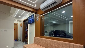 Un área de espera moderna con un banco, un reloj y un amplio ventanal que refleja un coche.