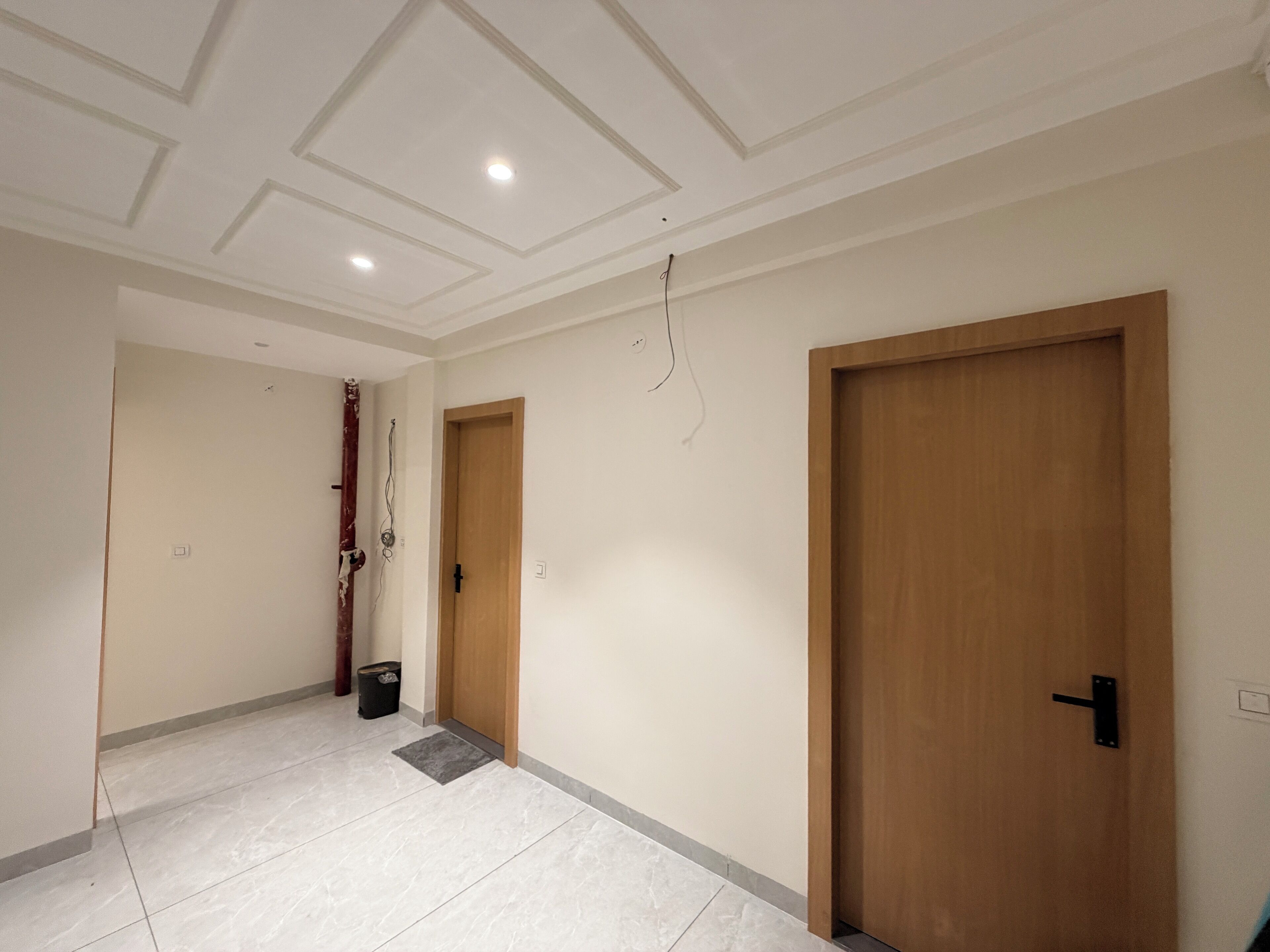 A hallway with two wooden doors, white walls, and a tiled floor.