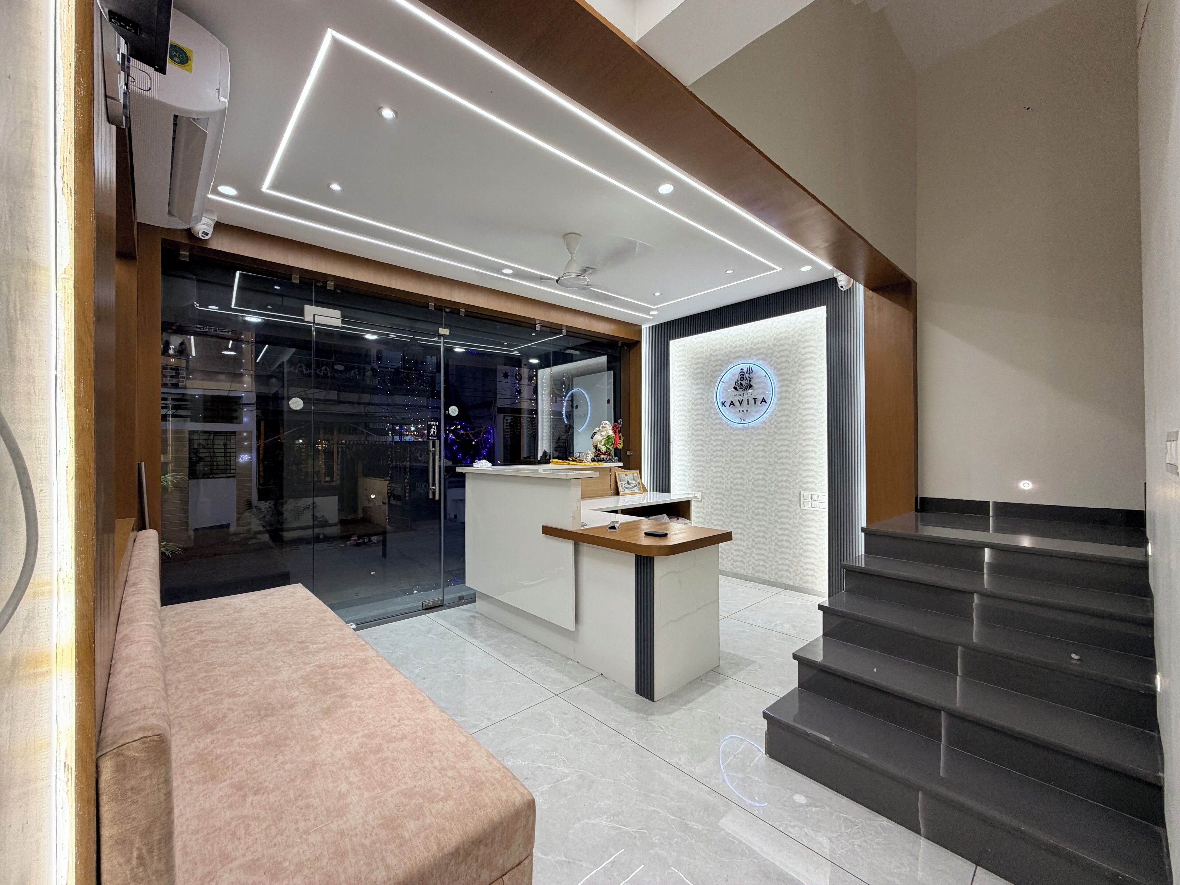 A modern hotel lobby with a reception desk, a staircase, and a glass wall leading to a dining area.
