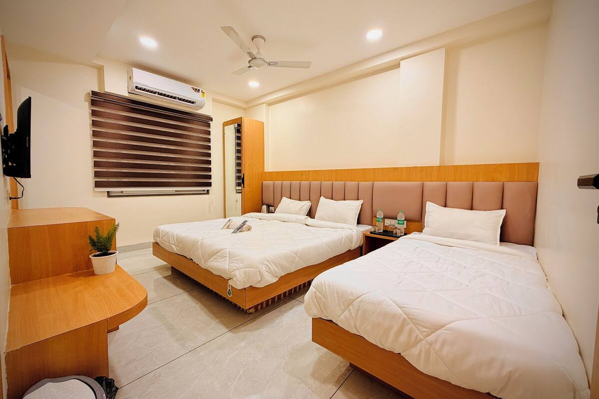 A hotel room with two beds, a desk, a mirror, an air conditioner, and a ceiling fan.