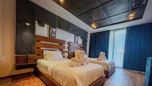 A hotel room with two beds, a wooden headboard, a large window with curtains, and a patterned rug. - ABM Green (Tangier)