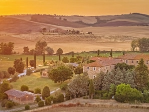 A rural landscape with rolling hills, a stone house, and a small building with a tiled roof. - Le Sorbelle D Orcia (Pienza)