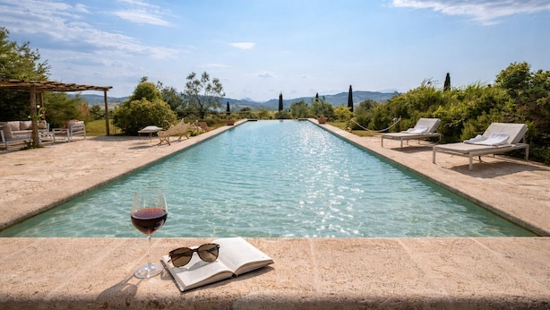 Ein Swimmingpool mit Liegestühlen, ein Glas Rotwein und ein offenes Buch am Rand.
