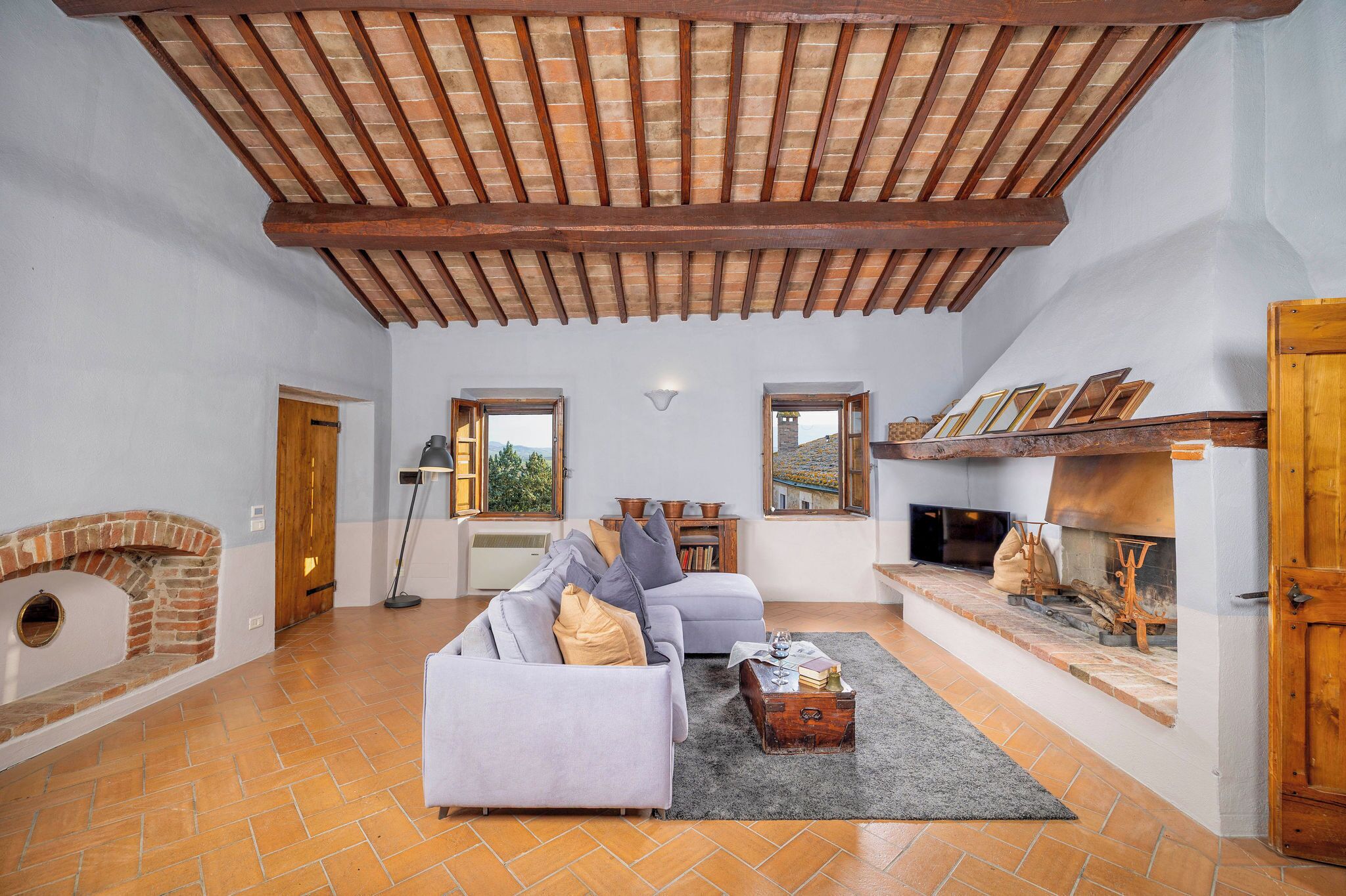 A spacious living room with a high wooden ceiling, a fireplace, and a sofa with cushions.