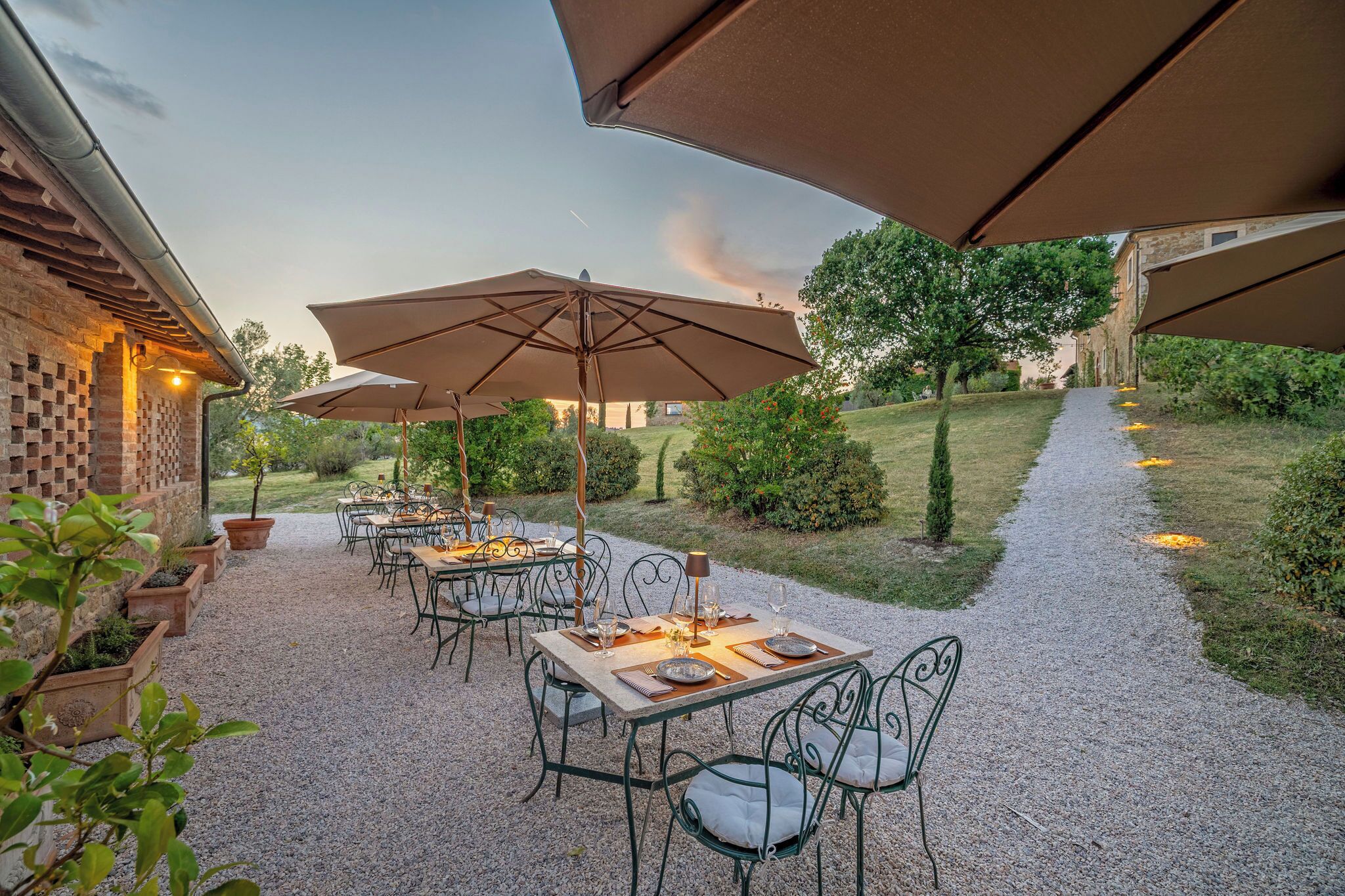 An outdoor patio with tables and chairs, umbrellas, and a gravel path.