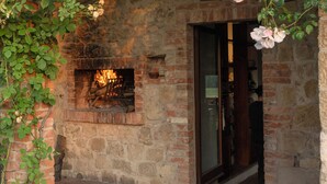 Ein rustikales Steinhaus mit Kamin aus Ziegelsteinen, einer Holzpergola mit Rosenranken und einem gefliesten Eingangsbereich.